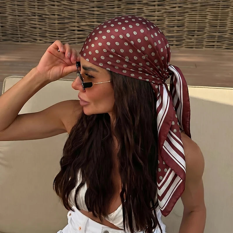 A woman wearing an elegant silk dot print scarf tied around her hair and neck.
