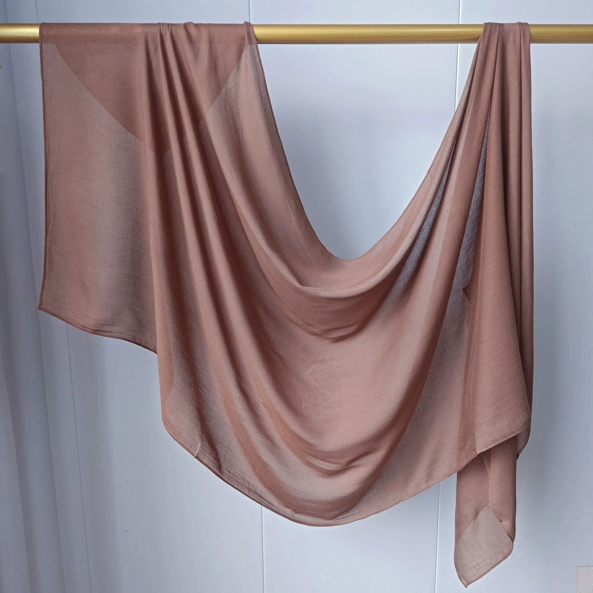Foulard hijab modal rose poudré, fluide et transparent, drapé sur un cintre en bois.