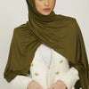 Eine Frau trägt einen olivgrünen Jersey-Hijab und einen weißen Blazer.