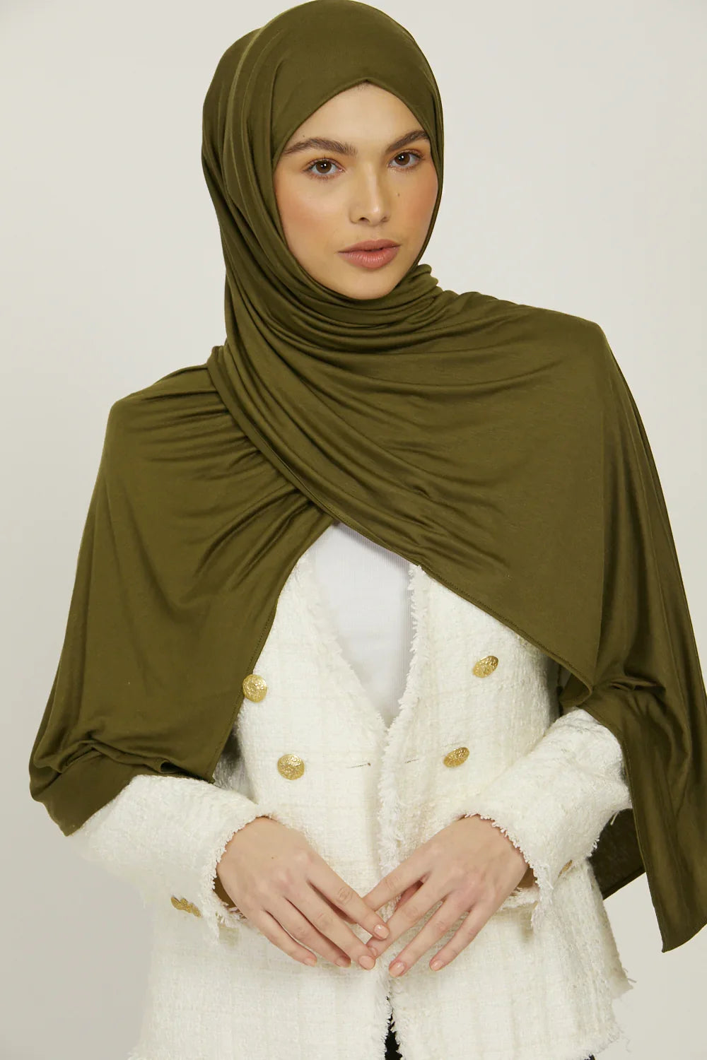 Eine Frau trägt einen olivgrünen Jersey-Hijab und einen weißen Blazer.
