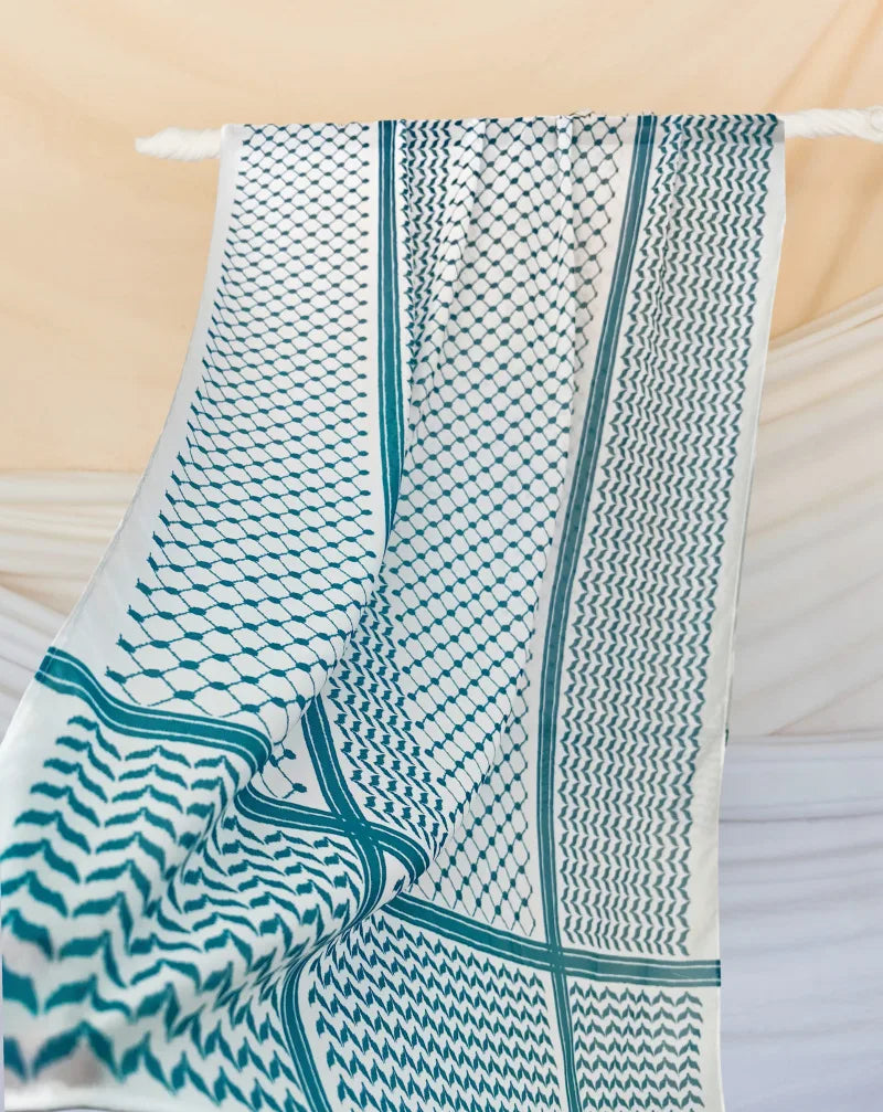 Hijab keffiyeh de gasa moteada en verde azulado y blanco colgada en un perchero contra un fondo claro.