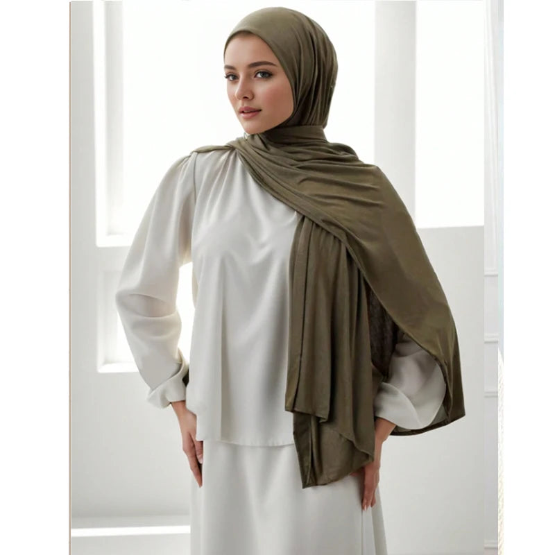 Eine Frau trägt einen olivgrünen Jersey-Schal als Kopftuch über einem weißen Oberteil und Kleid.