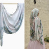 Eine Frau trägt einen hellvioletten Aquarell-Ombré-Hijabschal über Kopf und Schultern.