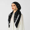 Eine Frau modelliert einen schwarz-satinierten Turban-Hijab mit weißen Polka-Punkten und Streifen über einem weißen Oberteil.