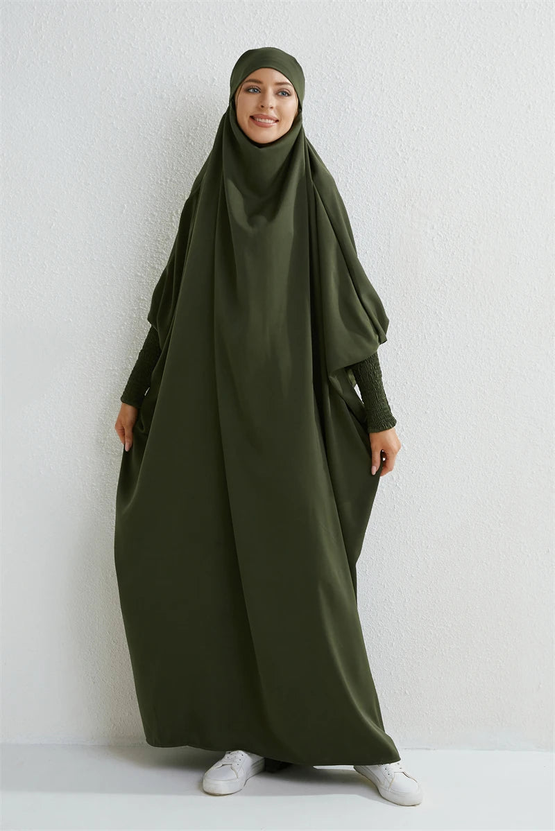 Eine Frau trägt eine olivgrüne, hochgeschlossene Abaya mit gerafften Ärmeln und einem passenden Hijab.