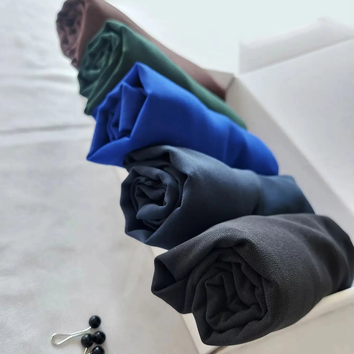 Pila de elegantes pañuelos de chifón de un solo color en tonos de verde, azul y gris.