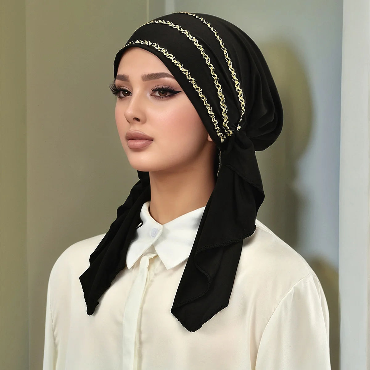 Eine Frau trägt einen schwarzen Hijab mit goldenen Streifen und einem weißen Shirt.