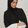 Eine Frau trägt einen schwarzen Jersey-Hijab und einen weißen Blazer.