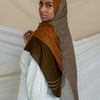 Una mujer vistiendo un pañuelo de hijab marrón y beige sobre una blusa blanca.