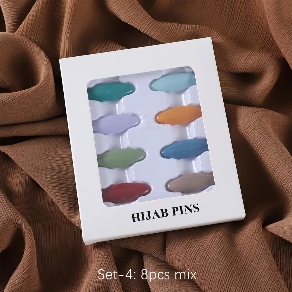 Ein Set von vier farbenfrohen Hijab-Pins in verschiedenen Schattierungen wird in einer weißen rechteckigen Box auf einem brau