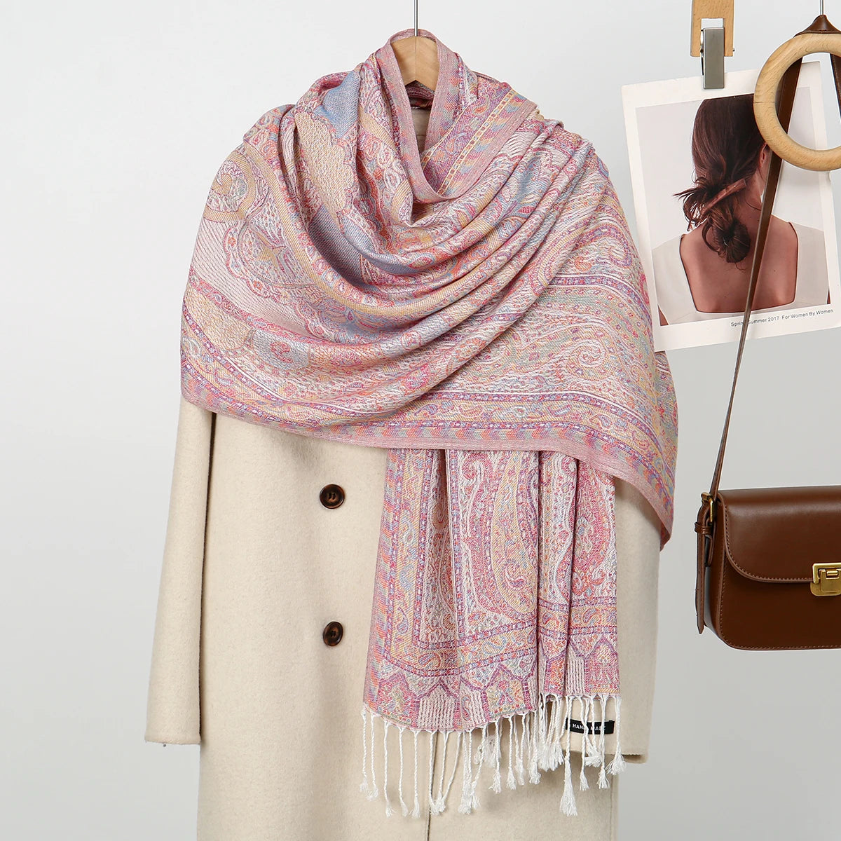 Un chal de bordado paisley rosa y morado drapeado sobre un abrigo beige, con una foto enmarcada a juego cerca.