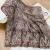 A brown and black leopard print silk satin scarf draped on a white surface.