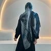 Eine Frau in schwarzem Outfit und einem blauen und grauen Aquarell-Blumenmuster-Hijabschal, von hinten gesehen.