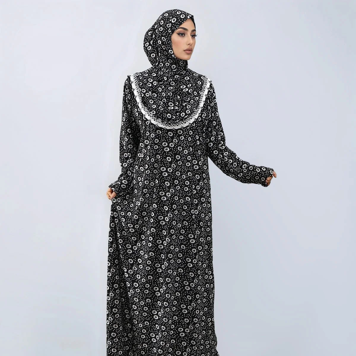 A woman wearing an elegant black and white patterned Muslim hijab dress with lace trim.