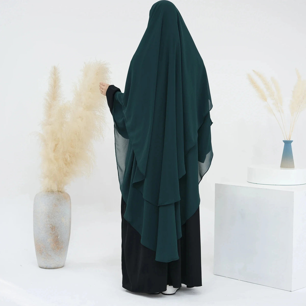 Dunkel-türkises, zweilagiges Chiffon-Niqab-Kopftuch, neben trockenem Ziergräser und einer weißen Box.