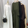 Elegante weiße Batwing-Abaya auf einem Mannequin mit verschiedenen bunten Kleidungsstücken im Hintergrund.