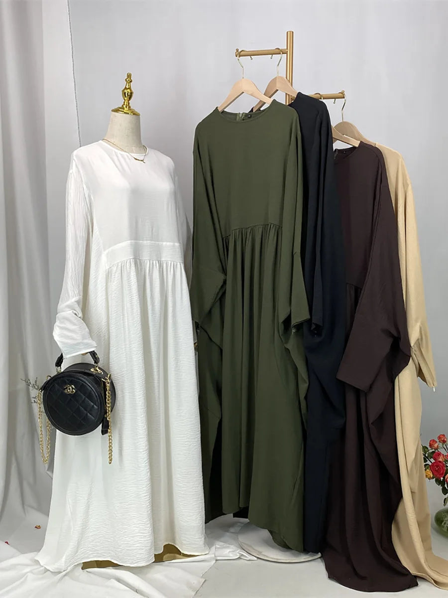 Elegante weiße Batwing-Abaya auf einem Mannequin mit verschiedenen bunten Kleidungsstücken im Hintergrund.