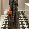 Une femme modèle un long trench coat sombre à motif plissé avec un sac orange sur fond à damier noir et blanc