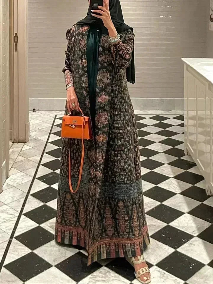 Une femme modèle un long trench coat sombre à motif plissé avec un sac orange sur fond à damier noir et blanc