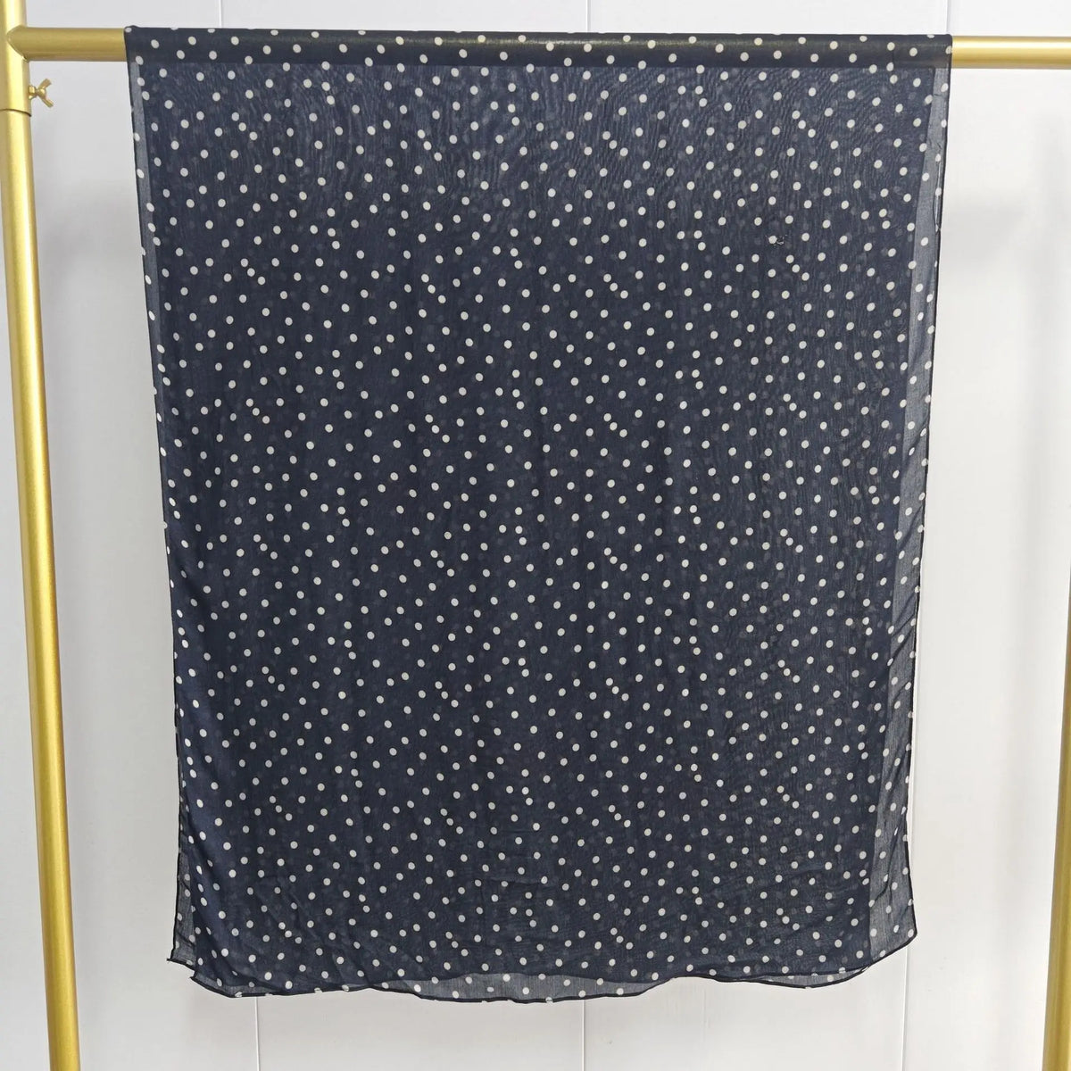 Dunkelblaue, durchscheinende Schal mit kleinen weißen Polkadotten an einem goldenen Haken.