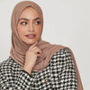 A woman wearing a beige stretchy jersey plain hijab scarf and a black and white patterned jacket.
