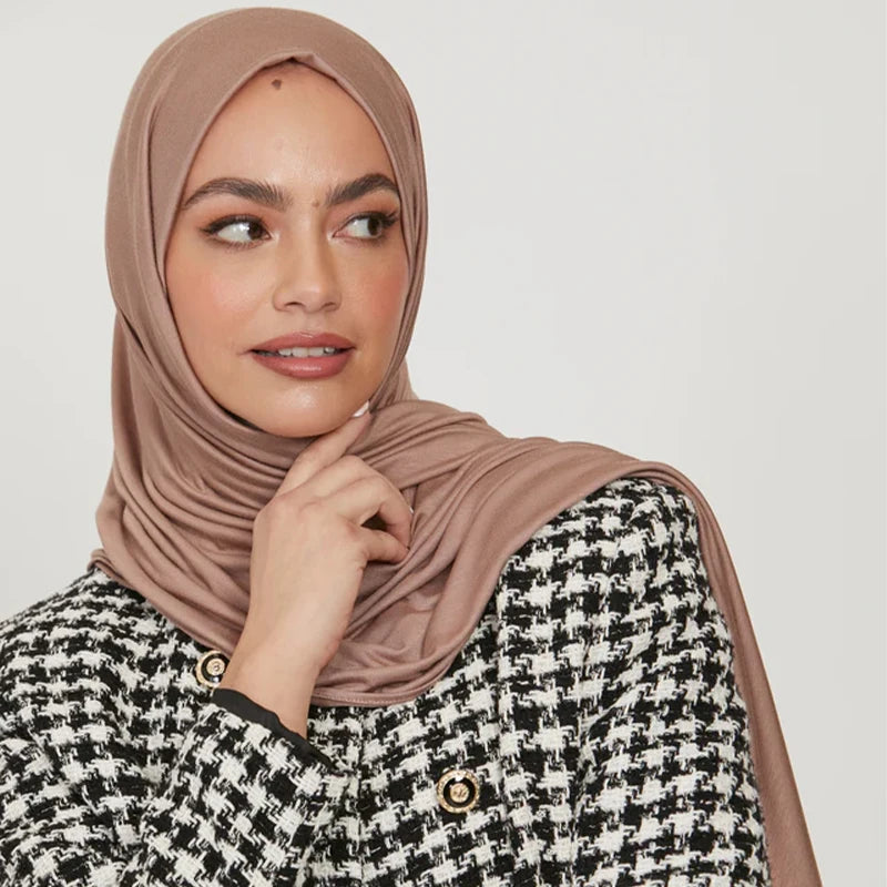 A woman wearing a beige stretchy jersey plain hijab scarf and a black and white patterned jacket.