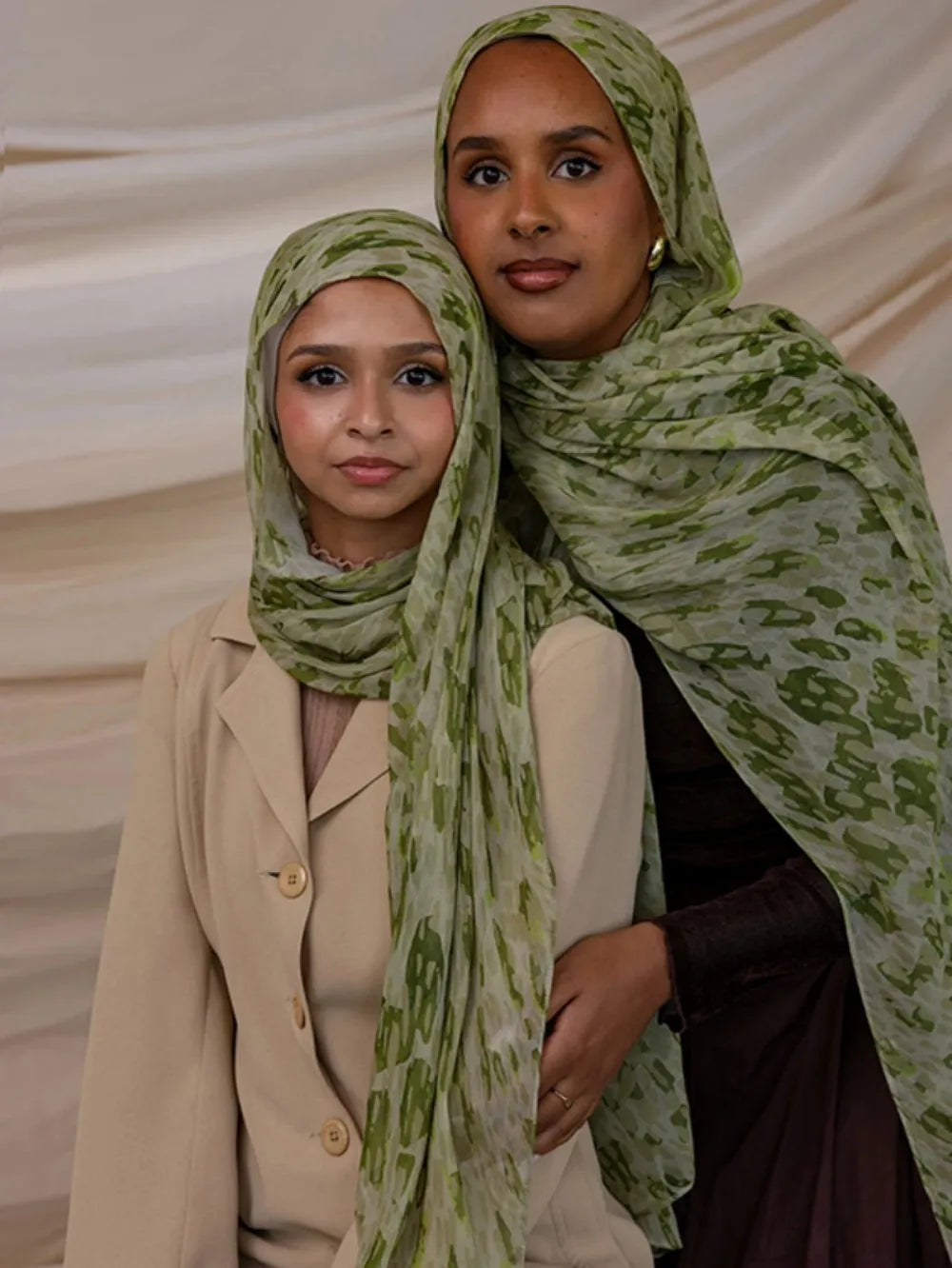 Une femme portant un foulard hijab à motifs verts et blancs et un blazer beige.