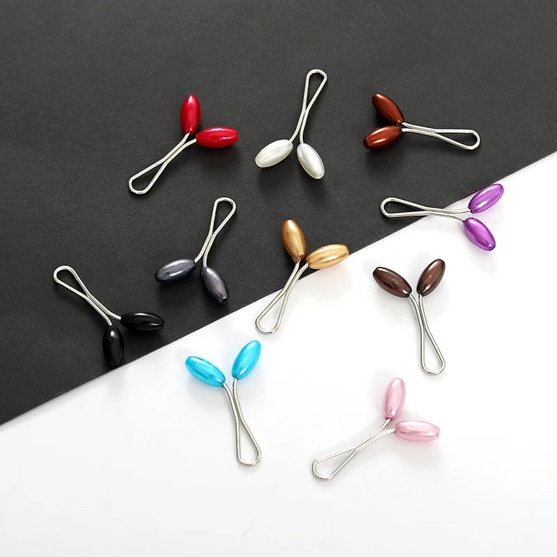 A collection of twelve pearl-colored brooch headscarf pins in various shades and finishes.