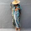 Eine Frau trägt einen blau-braunen gemusterten Kimono-Überwurf über einem schwarzen Top und hellgewaschenen Jeans mit Strohhu