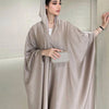 Una mujer vistiendo una abaya de satén beige con mangas de murciélago y un clutch plateado.