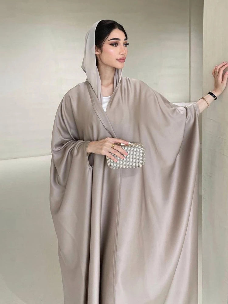 Una mujer vistiendo una abaya de satén beige con mangas de murciélago y un clutch plateado.