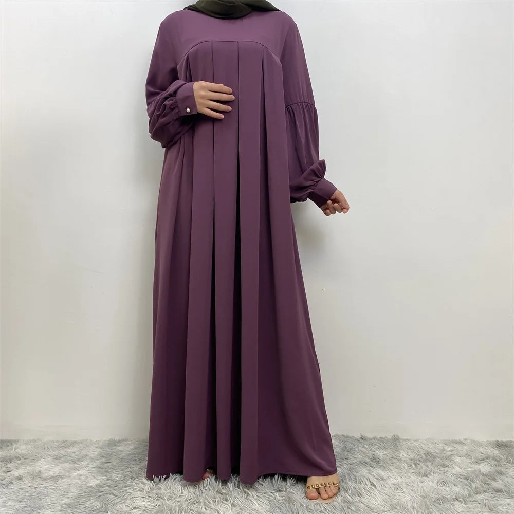 Eine Frau in einem eleganten, langen lila islamischen Kleid mit Hijab vor weißem Hintergrund.