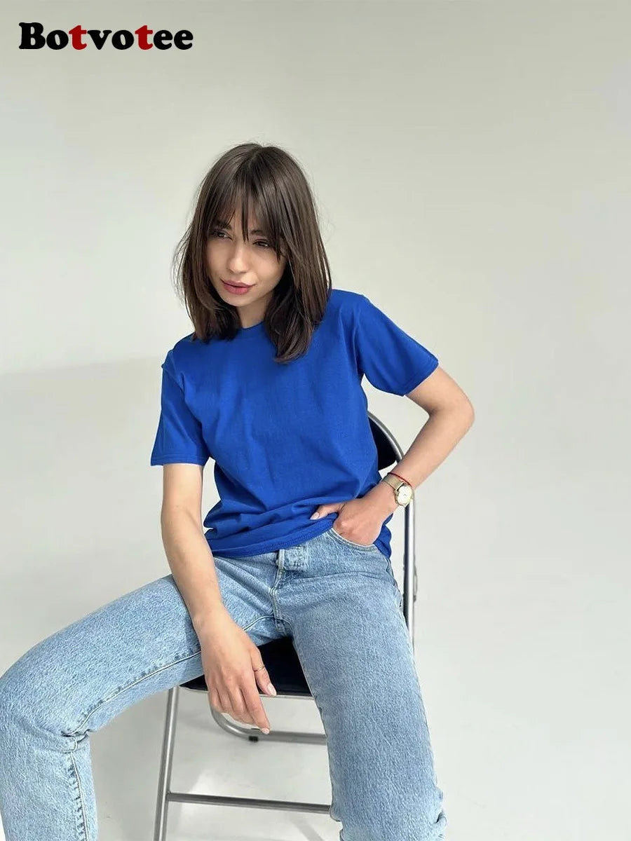 Una mujer vistiendo una camiseta básica de algodón azul real oversize y jeans de lavado claro, sentada en una silla.