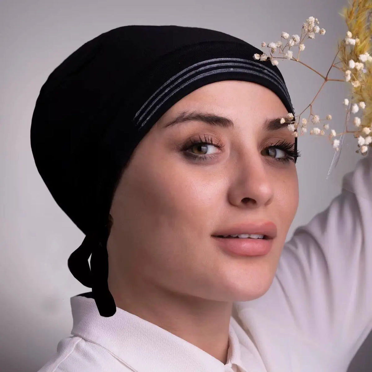 Une femme portant un foulard instant en tissu extensible noir avec des rayures argentées sur un fond clair.