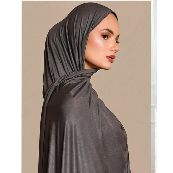 A model wearing a solid gray jersey scarf head wrap draped over her head and neck.