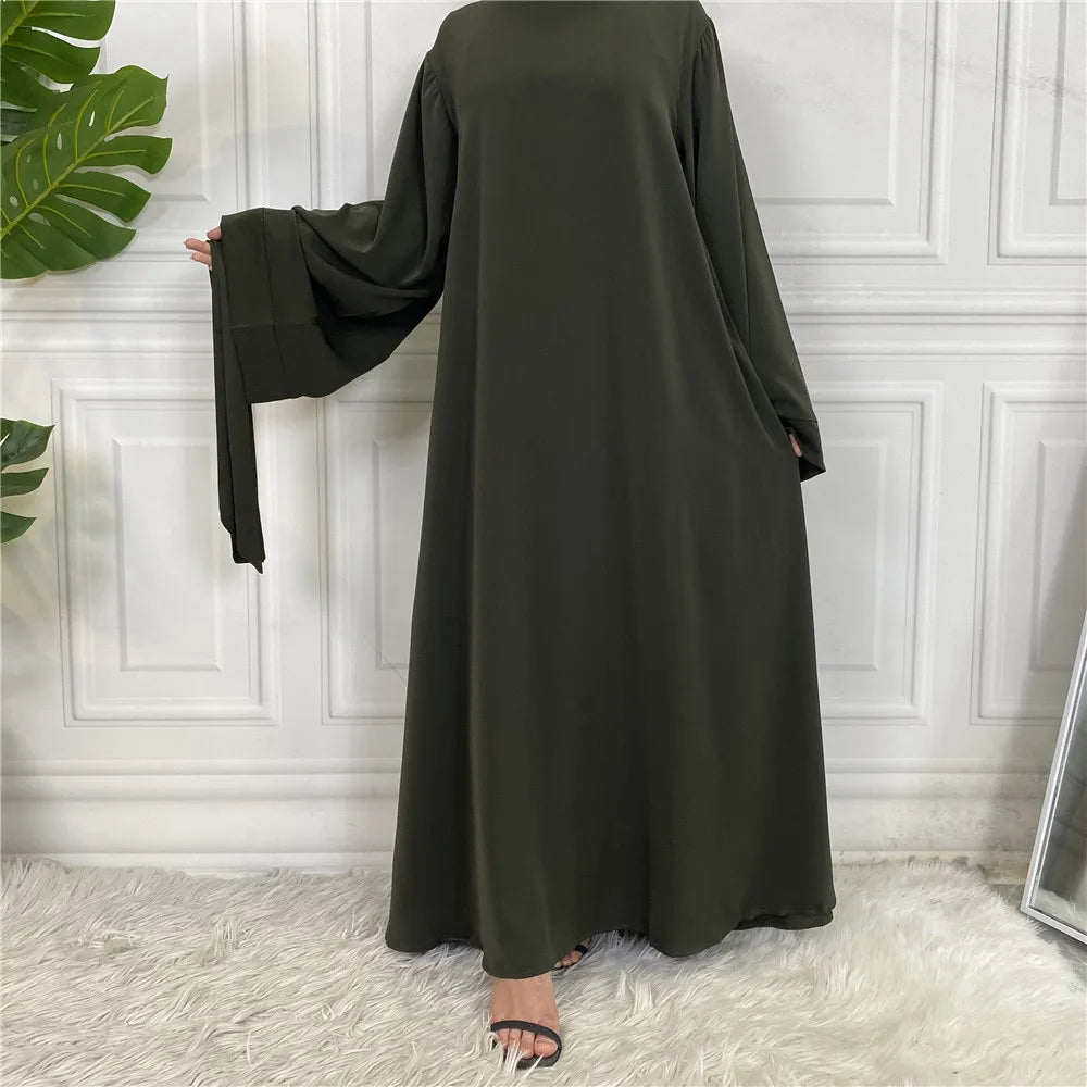 Elegante, dunkelolivgrüne Maxi-Abaya für Damen vor einer weißen Paneelwand.