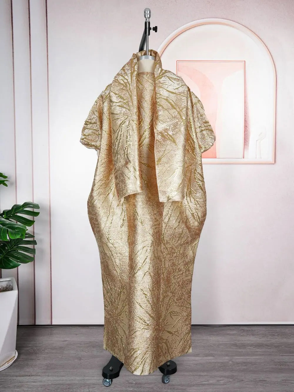 Vestido maxi dashiki de lentejuelas doradas completo en maniquí contra una pared rosa.