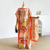 Eine Frau modelliert ein lockeres Sommerkaftan-Kleid mit orange-rosa Blumenmuster und einem Schal.