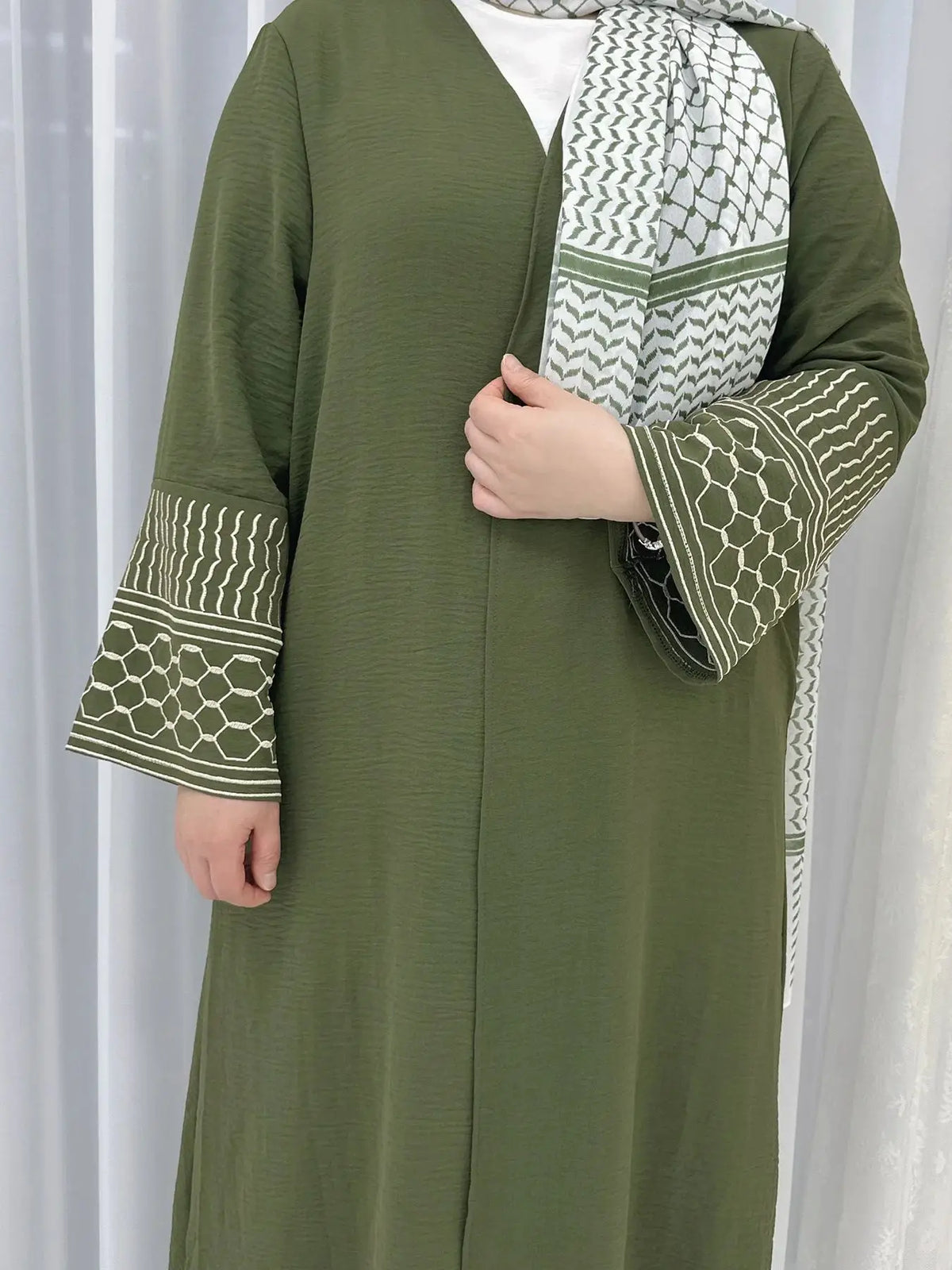Une femme portant une abaya vert olive avec un foulard à motifs et des manches brodées.