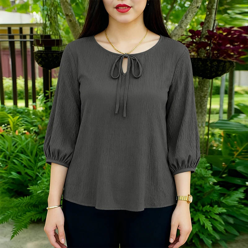 Eine Frau modelliert eine graue, langärmelige Bluse mit Knopfleiste in einer Gartenumgebung.