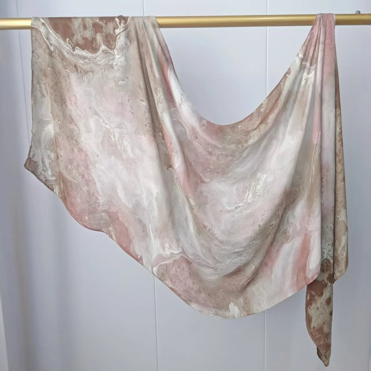 Fließender, mehrfarbiger Hijab-Schal drapiert über einem goldenen Haken vor weißem Hintergrund.