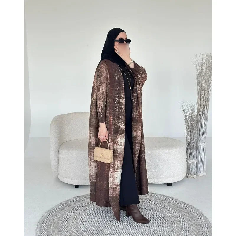 Une femme portant un trench-coat à manches longues à plis marron et des vêtements noirs se tient dans une pièce lumineuse.