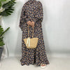 Una mujer vistiendo una elegante caftán abaya floral de manga larga y un bolso de paja.