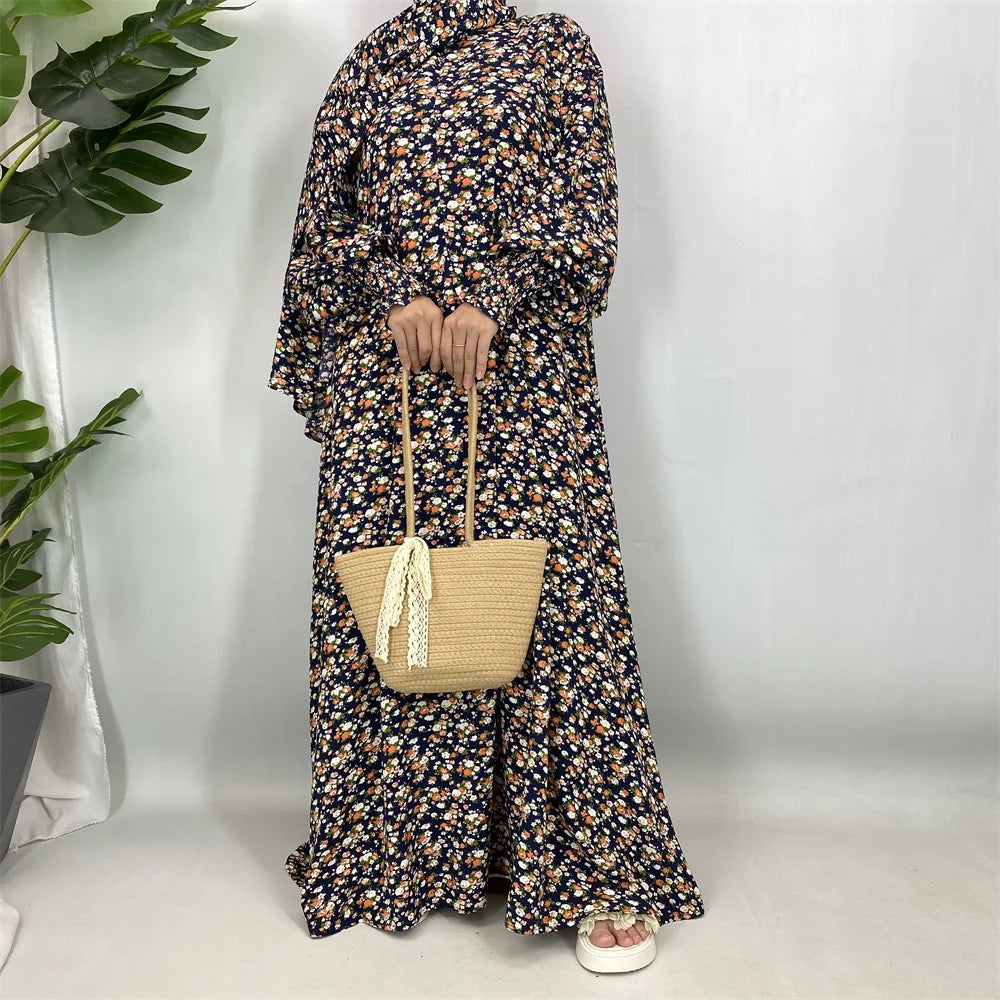 Una mujer vistiendo una elegante caftán abaya floral de manga larga y un bolso de paja.