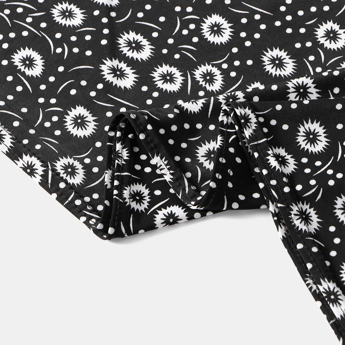 Black fabric with white floral and polka dot pattern, showing a folded section of an elegant Muslim hijab dress.