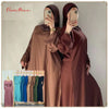 Eine Frau modelliert eine fließende, bordeauxrote Abaya mit weit ausgestellten Ärmeln und hält ihr Handy.