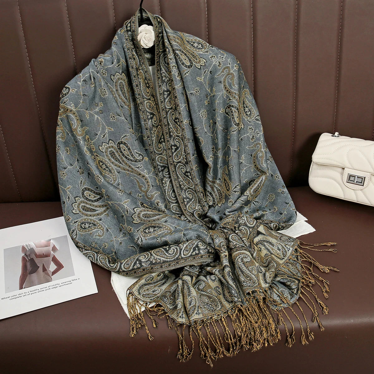 Una pashmina de lujo con estampado gris drapeada sobre una superficie de cuero marrón.
