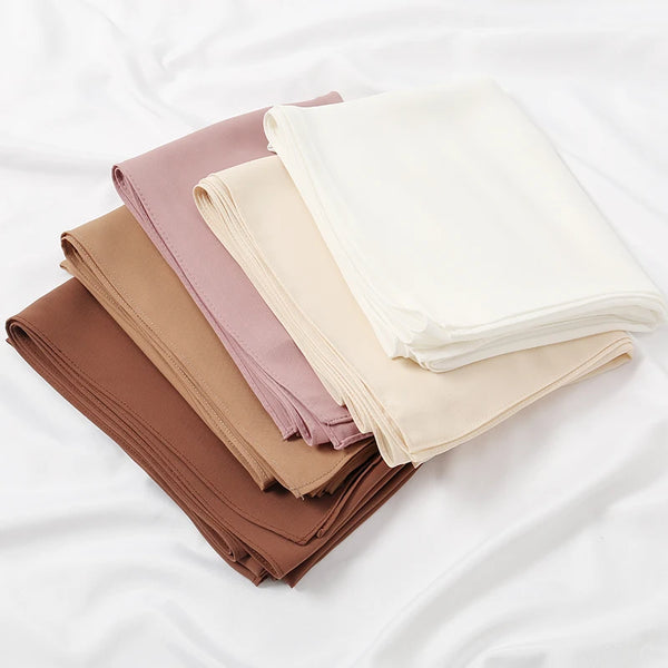 A stack of premium chiffon hijab scarves in various shades of beige, pink, and brown fabric.
