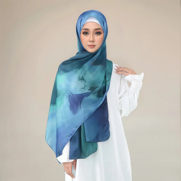 A woman wearing a blue and teal shimmer satin silk hijab shawl over a white outfit.