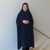 Eine Frau in eleganter dunkelblauer Baumwollabaya und Hijab vor einer hellen Wand.